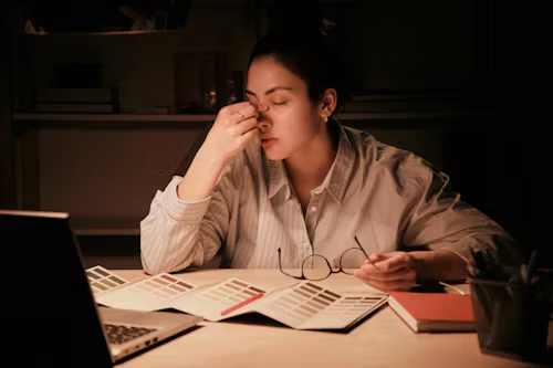 Student sitting at a desk looking tired and overwhelmed while studying late with a laptop and papers